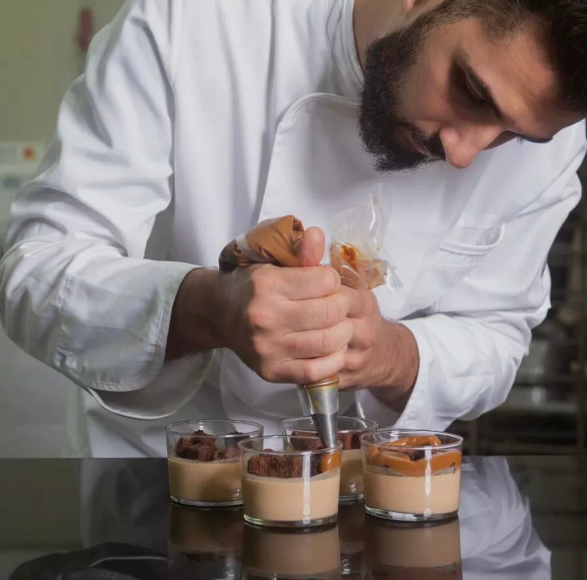 Chef pâtissier utilisant une poche à douille pour garnir des verrines de dessert au caramel.