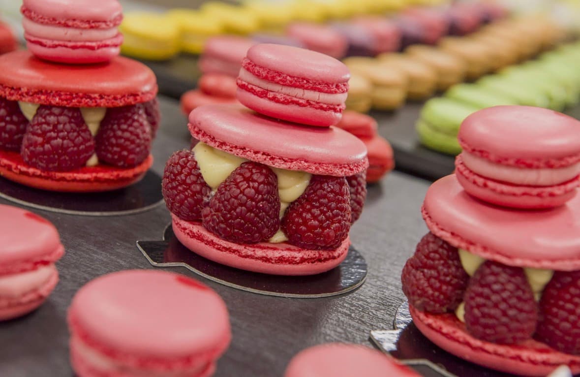 Macarons roses garnis de framboises fraîches et crème vanille, surmontés d'un petit macaron rose.