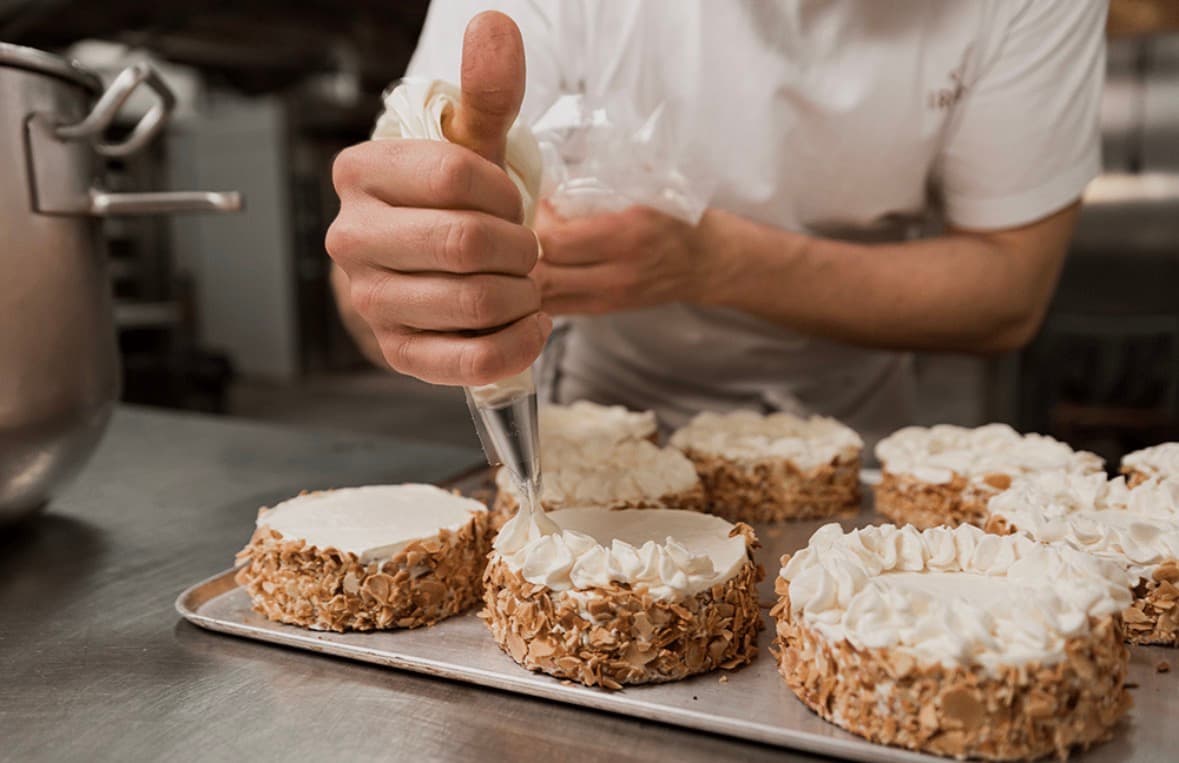 Un pâtissier utilisant une poche à douille pour décorer des gâteaux aux amandes effilées.